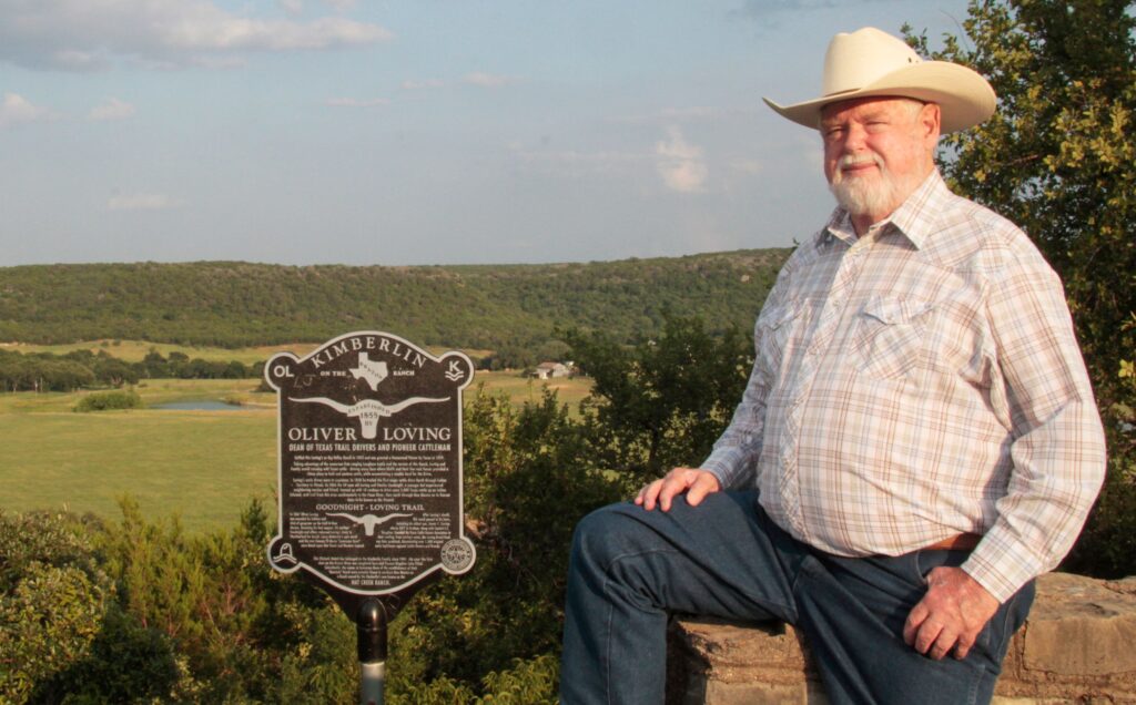 A man in cowboy hat sitting next to a sign.