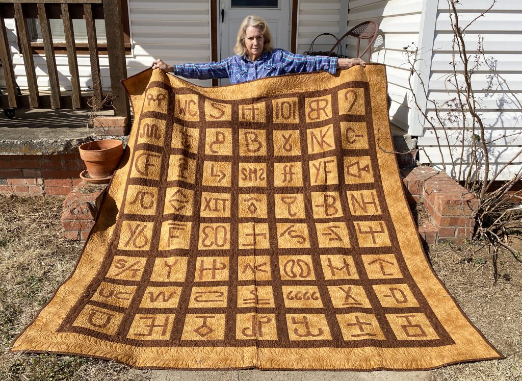 A person sitting in front of a quilt with the letters of the alphabet on it.