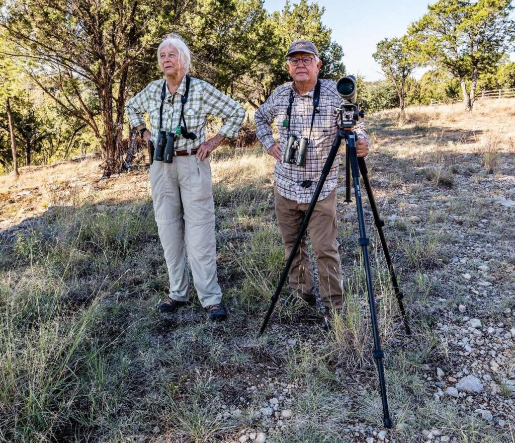 A man and woman standing in the grass with cameras.