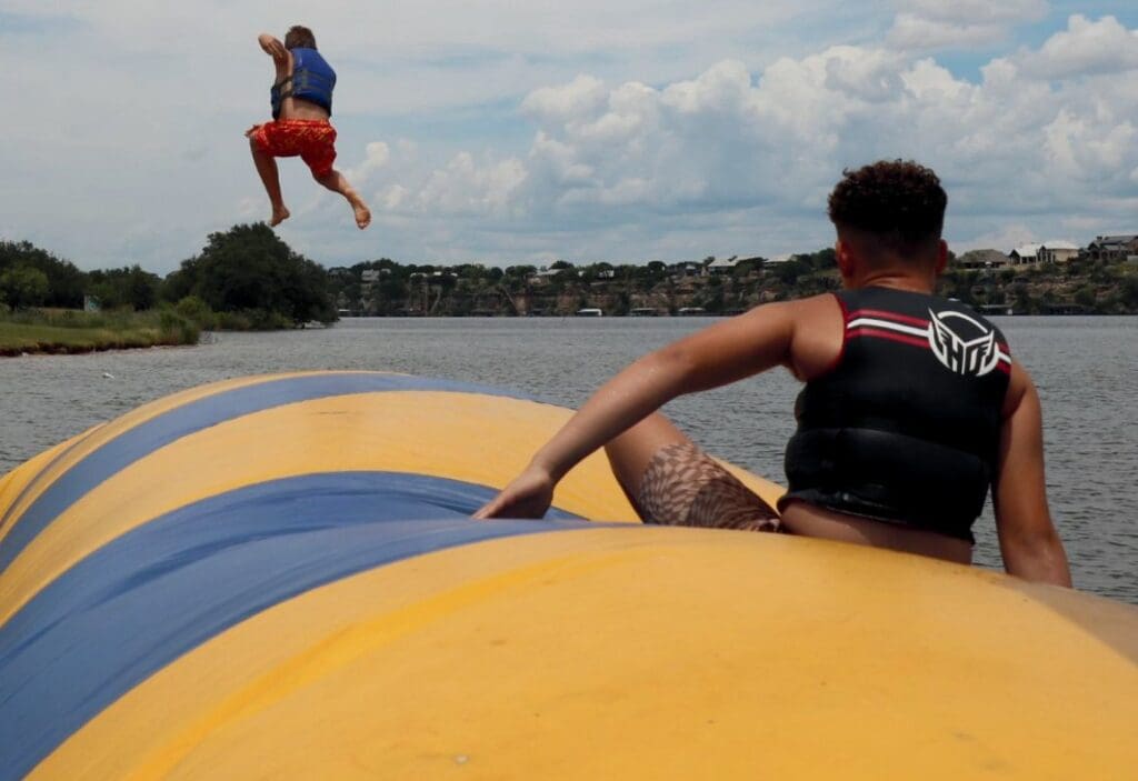 Children playing on a large inflatable water trampoline on a lake.