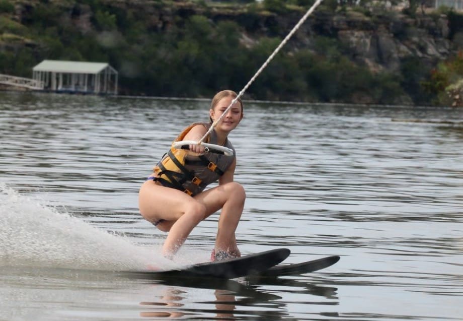 A person waterskiing on a calm lake, wearing a life jacket.