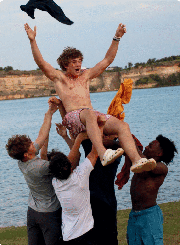 A group of friends lifting one person joyfully near a lake.