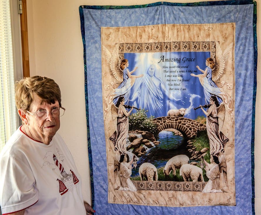 Elderly woman showcasing a detailed tapestry with animals and nature.