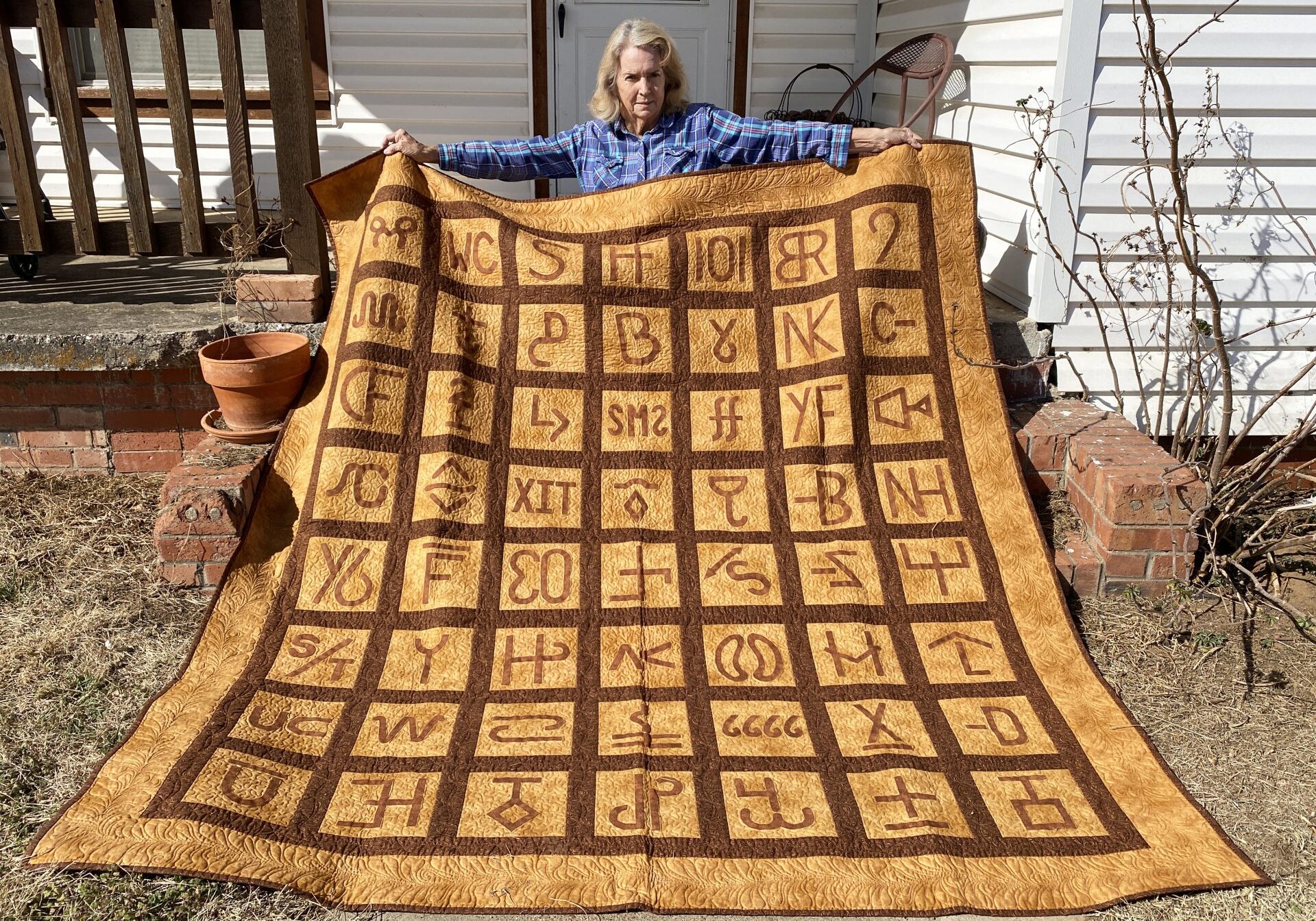 A person sitting in front of a quilt with the letters of the alphabet on it.