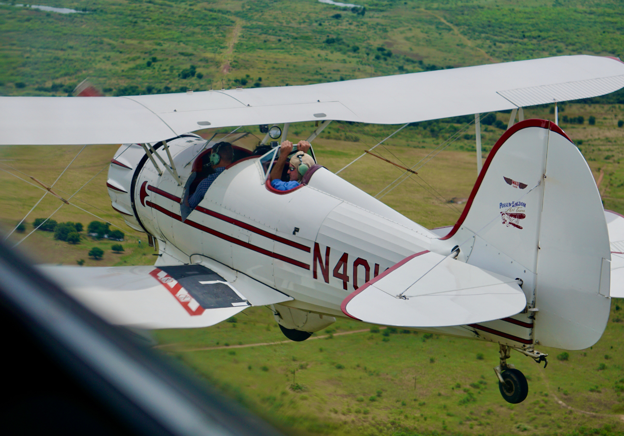 A small airplane flying over a lush green field.