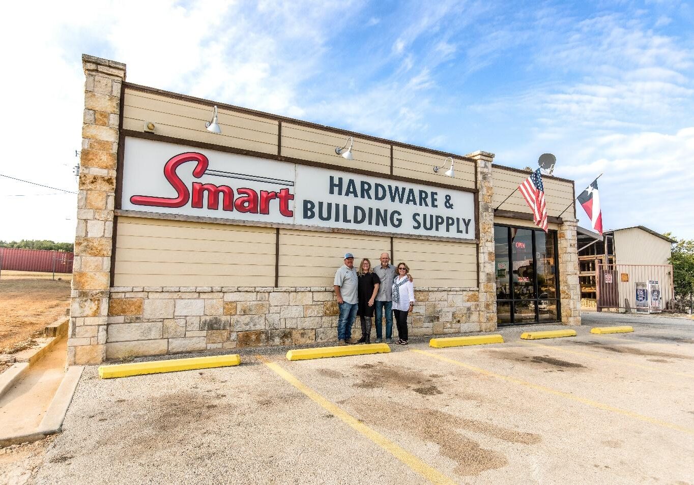 Three people standing in front of a building with the smart hardware & building supply sign on it.