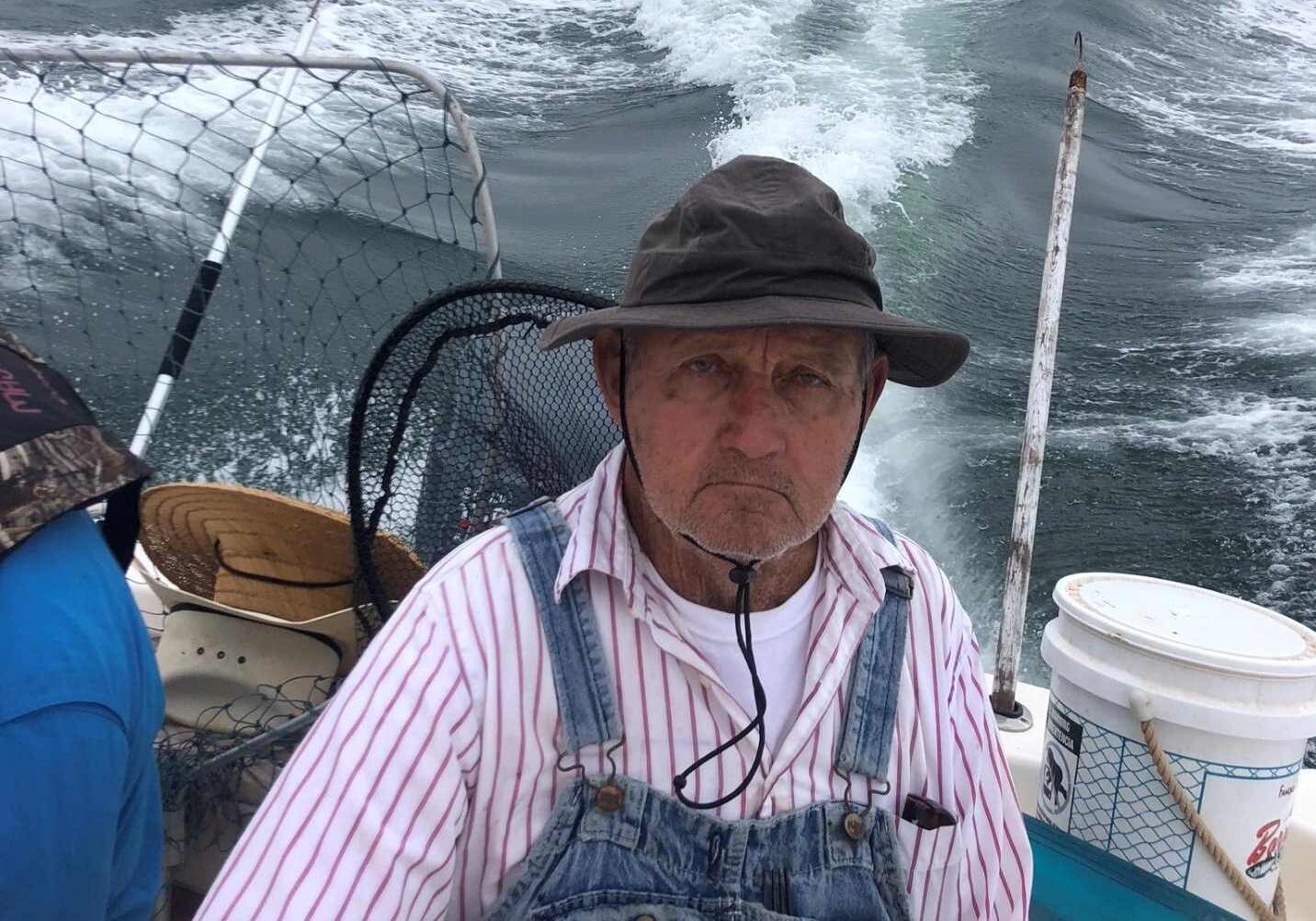 A man in an overalls and hat standing on the deck of a boat.