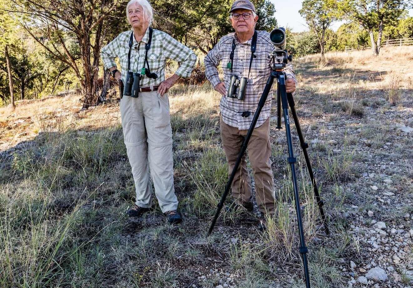 A man and woman standing in the grass with cameras.